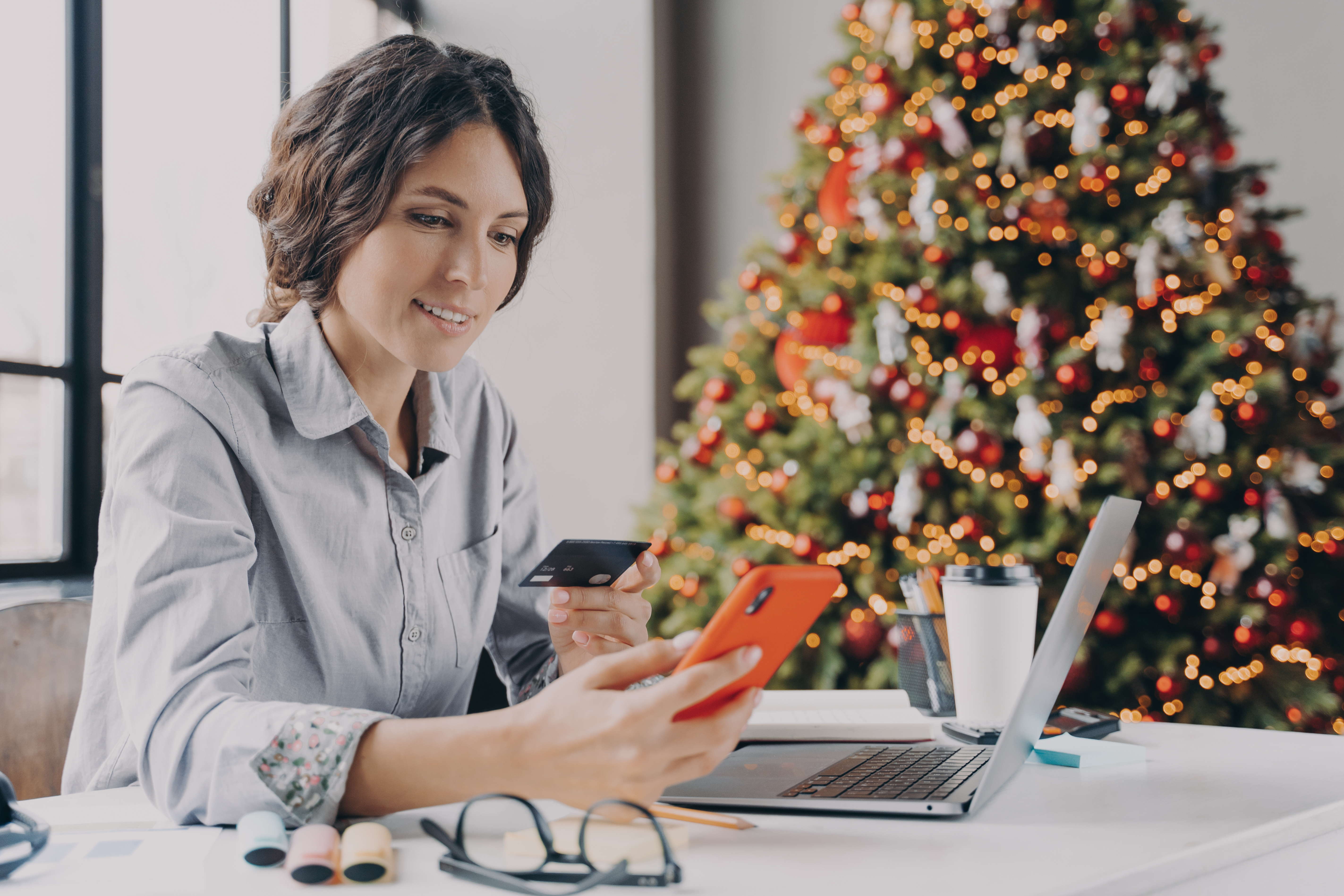 Spanish businesswoman holding credit card, doing online shopping on smartphone during Christmas time Find the best christmas deals
